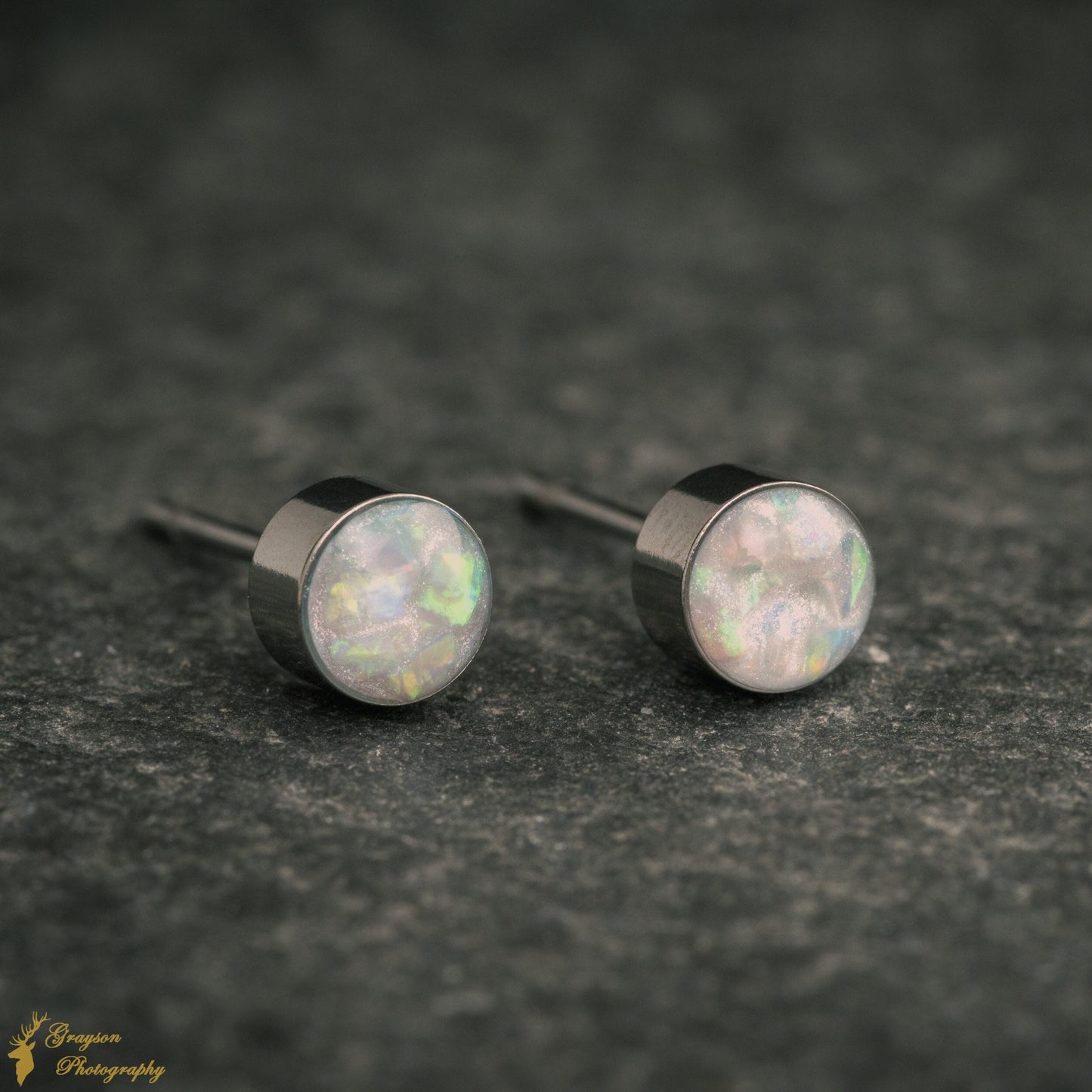 Silver coloured steel stud earrings with blue tinted white opal inlay. The studs are round and 5mm in diameter.